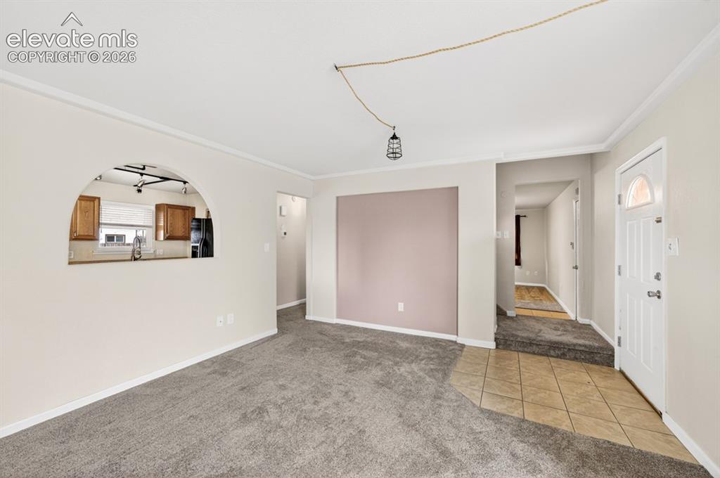 Image 7 of 25: Carpeted living area with crown molding, arched passthrough to kitchen, and