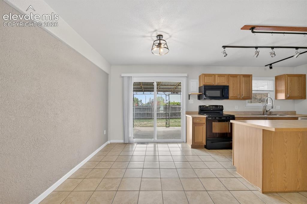 Image 8 of 25: Kitchen featuring wood cabinetry, black appliances, a central island, and t