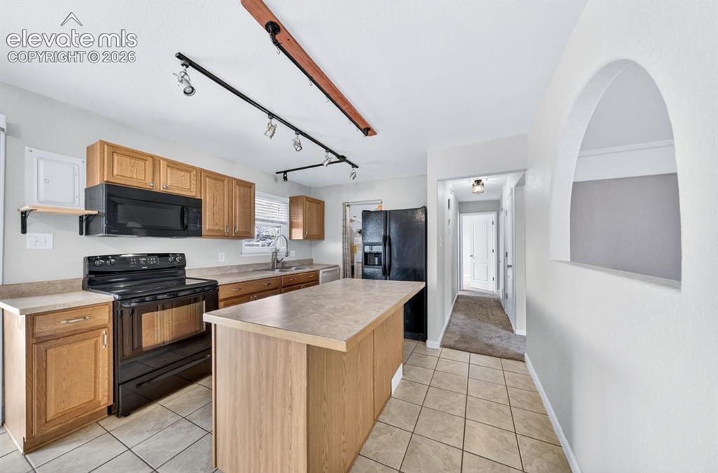 Image 9 of 25: Kitchen featuring wood-finish cabinetry, black appliances, track lighting,