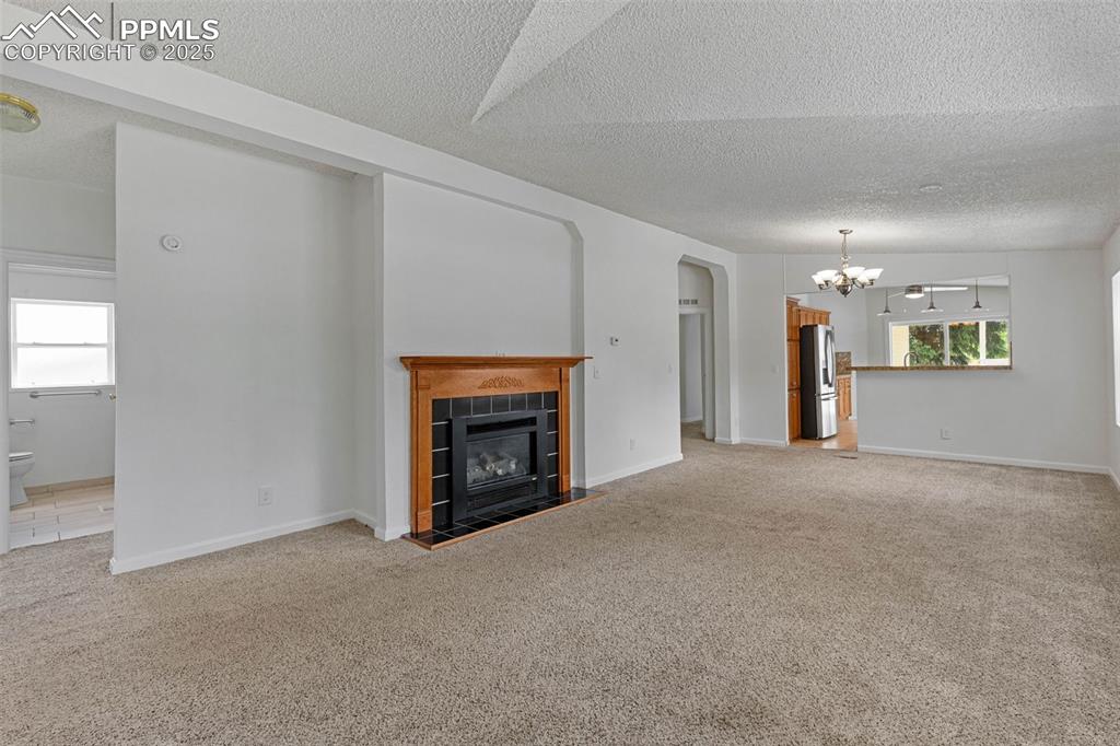 Image 11 of 24: Unfurnished great room featuring a chandelier, a tiled fireplace, a texture