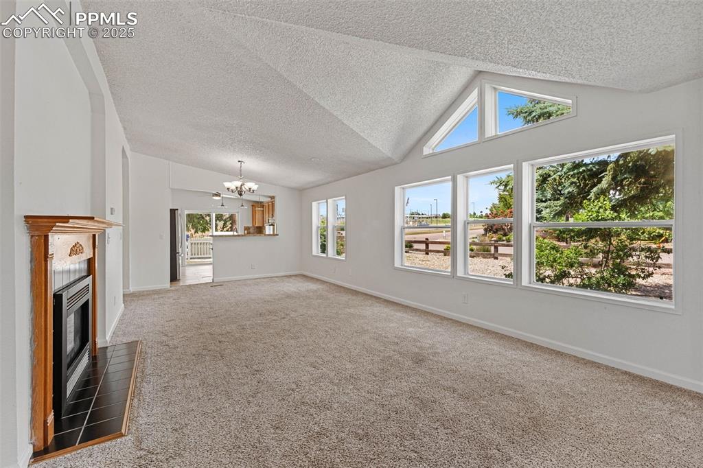 Image 12 of 24: Unfurnished living room with a chandelier, a textured ceiling, carpet, a fi