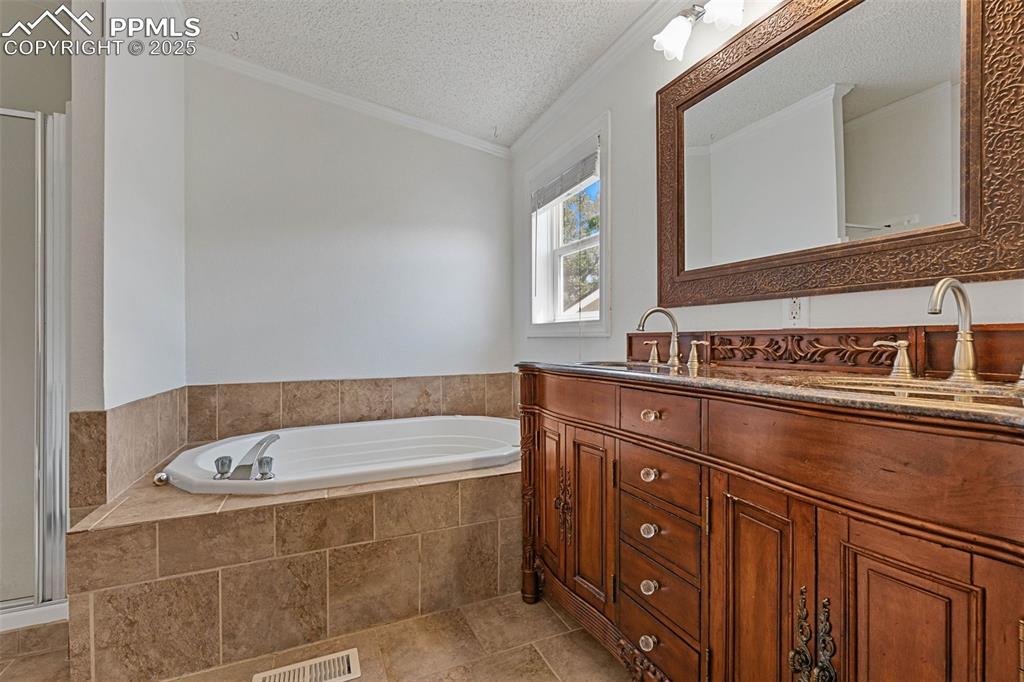 Image 18 of 24: Full bath with vanity, a bath, a textured ceiling, ornamental molding, and 