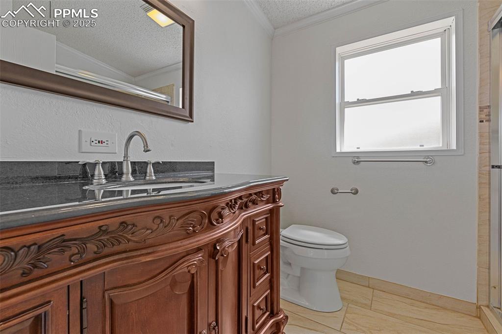 Image 20 of 24: 3/4 bathroom with ornamental molding, vanity, a textured ceiling, and a sho