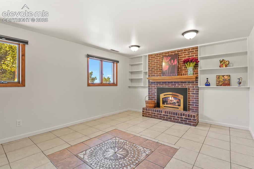 Image 21 of 50: Lower level family room with brick fireplace hearth & decorator tile medall