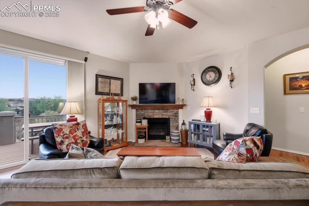 Image 12 of 26: Living room with wood finished floors, a stone fireplace, ceiling fan, and