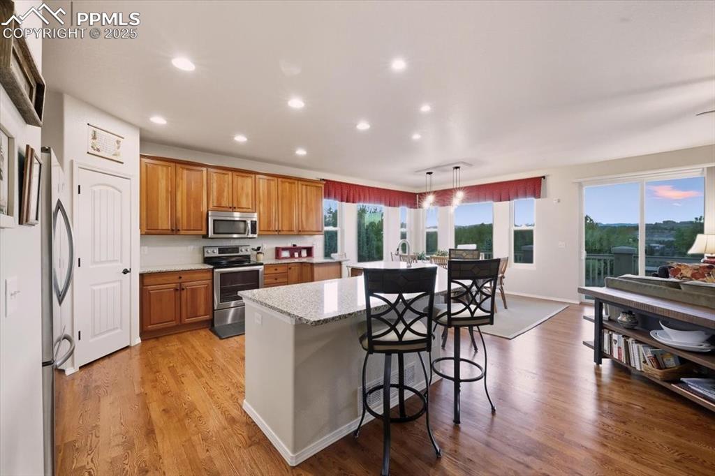 Image 7 of 26: Kitchen with a kitchen bar, brown cabinets, stainless steel appliances, lig