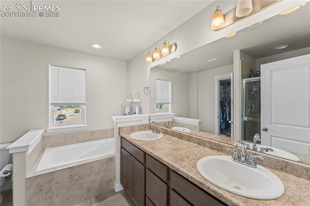 Image 13 of 33: Bathroom with a walk in closet, a shower stall, a bath, double vanity, and