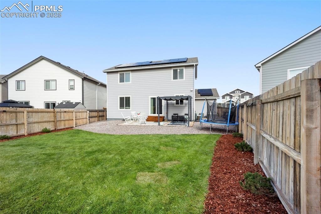 Image 28 of 45: Back of house with solar panels, a patio, a trampoline, and a fenced backya