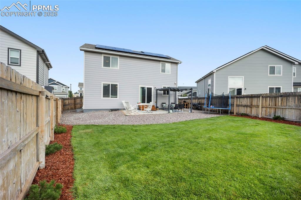 Image 30 of 45: Rear view of house with a patio area, roof mounted solar panels, a trampoli