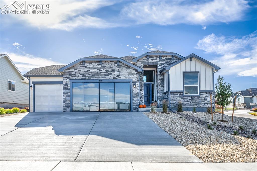 Caption: View of front of house with a garage, board and batten siding, stone siding, and concrete driveway