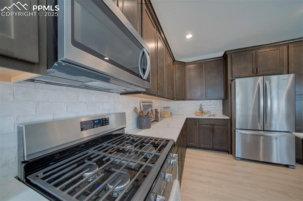 Image 12 of 44: Kitchen featuring light stone countertops, dark brown cabinetry, appliances