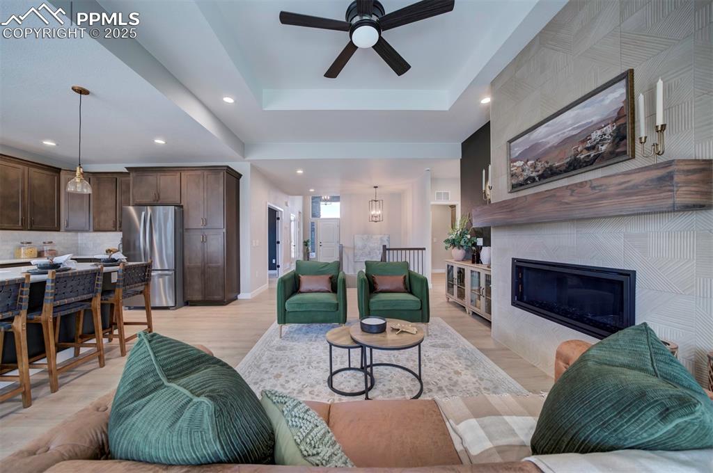 Image 6 of 44: Living area featuring a ceiling fan, baseboards, a raised ceiling, light wo