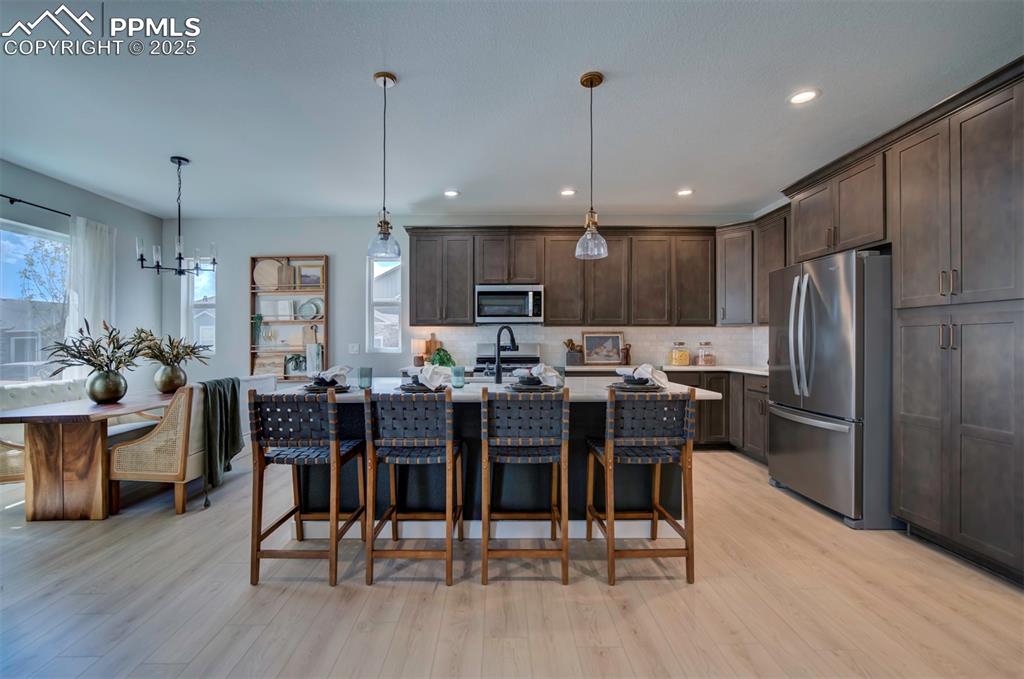 Image 8 of 44: Kitchen with dark brown cabinetry, light wood-style floors, light counterto