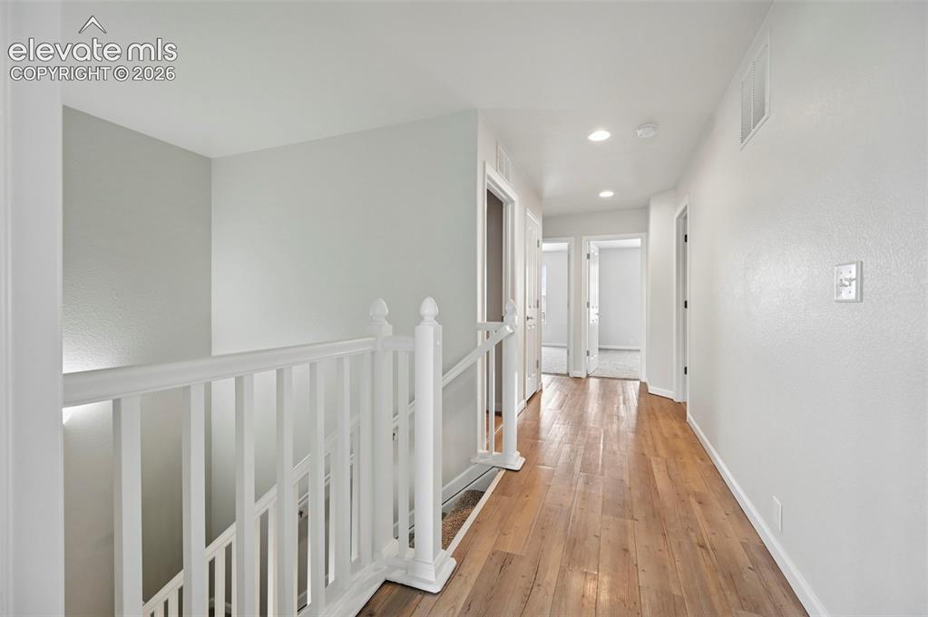 Image 16 of 33: Upper-level hallway featuring wood-finish flooring, white walls, recessed l