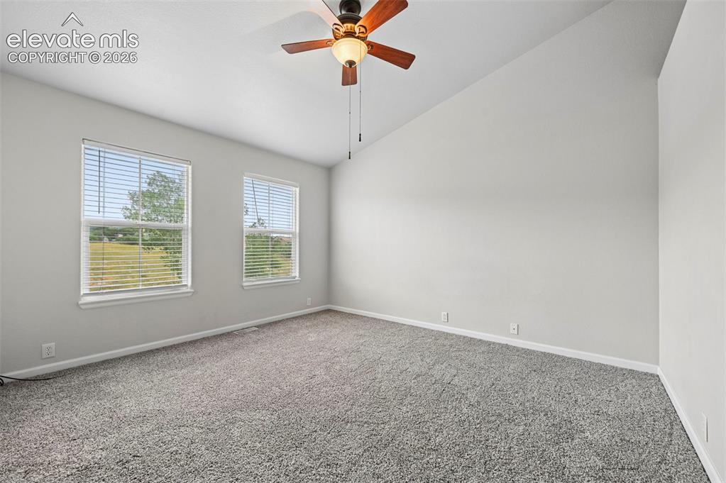Image 9 of 33: Spacious room featuring vaulted ceilings, a ceiling fan with light fixture,