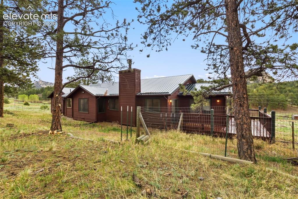 Image 27 of 29: Rear exterior surrounded by mature pines with expansive outdoor space, deck