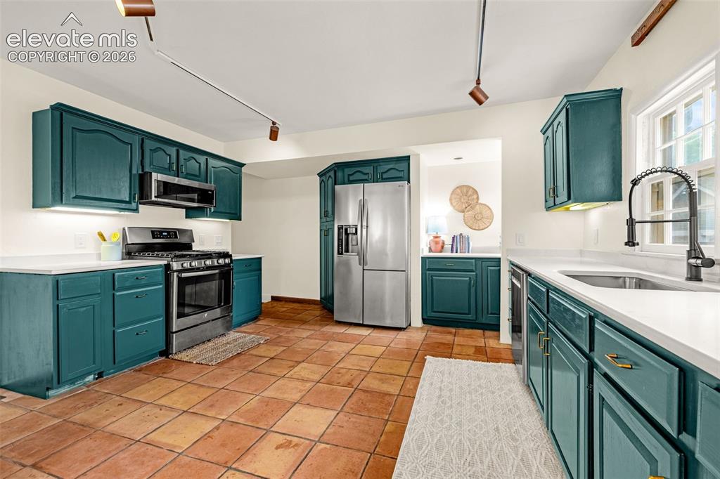 Image 14 of 50: Kitchen featuring teal cabinetry, white countertops, stainless steel applia