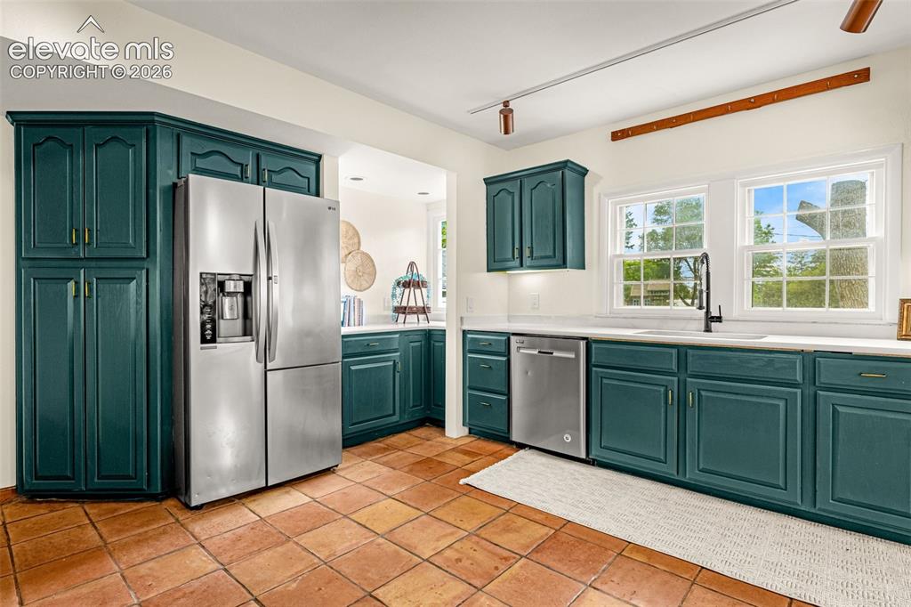 Image 16 of 50: Kitchen featuring teal cabinetry, stainless steel appliances, white counter