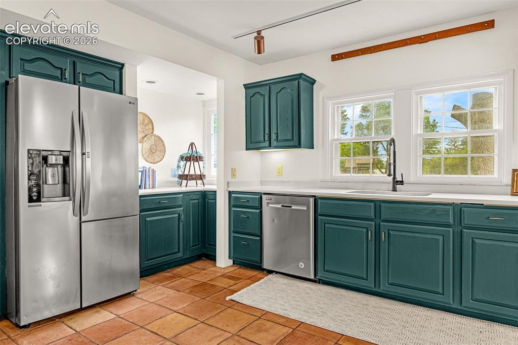 Image 17 of 50: Kitchen featuring teal cabinetry, stainless steel appliances, white counter