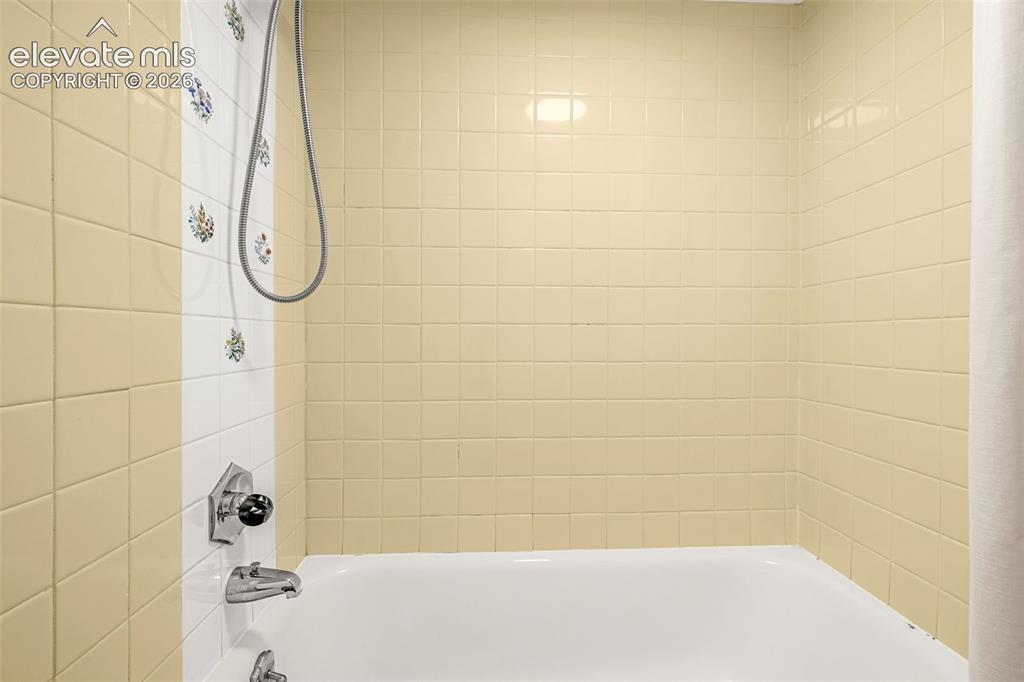 Image 24 of 50: White bathtub with a chrome faucet, shower head, and yellow tiled walls fea
