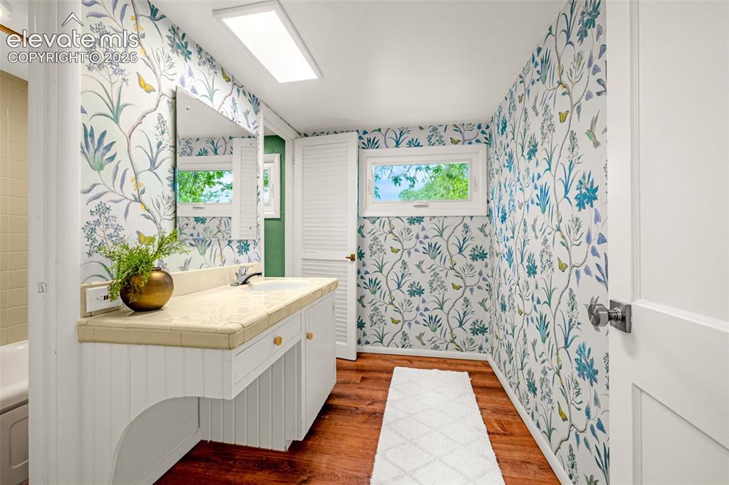Image 30 of 50: Wood-finish flooring, white vanity with beadboard paneling, tile countertop