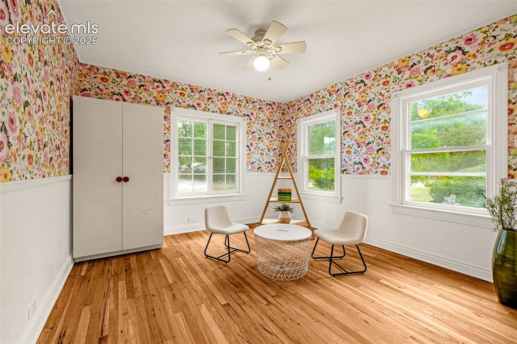 Image 34 of 50: Hardwood flooring, multiple windows, ceiling fan, white paneled wainscoting