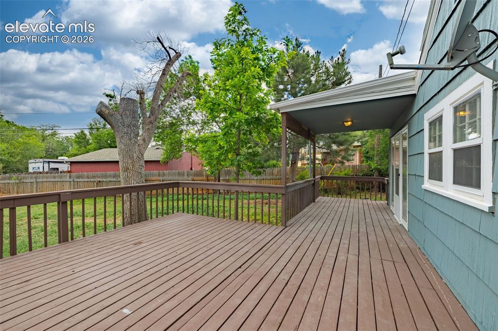 Image 39 of 50: Expansive wooden deck with railing, covered porch, and blue siding exterior