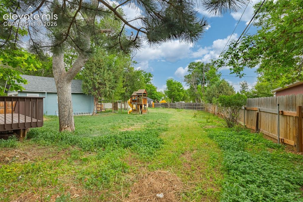 Image 49 of 50: Expansive backyard featuring a wood deck, mature trees, and privacy fencing