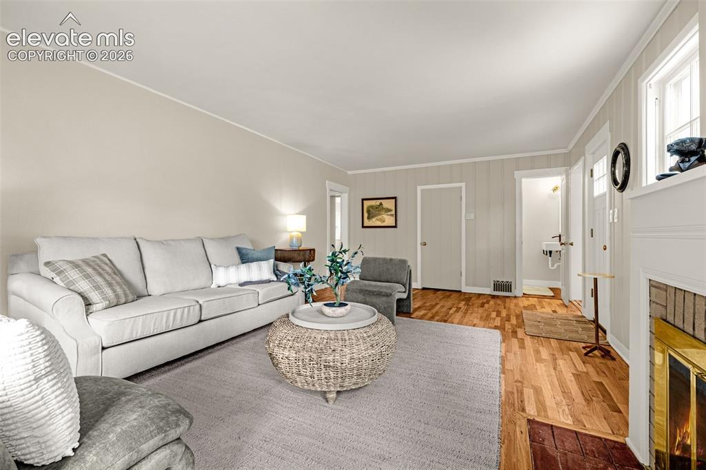 Image 5 of 50: Hardwood flooring, white trim, and a fireplace with a brass firebox