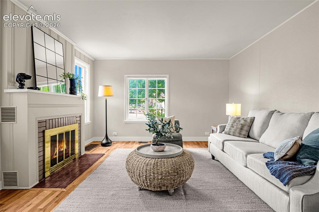 Image 8 of 50: Living room with wood-finish flooring, a fireplace featuring a brick surrou