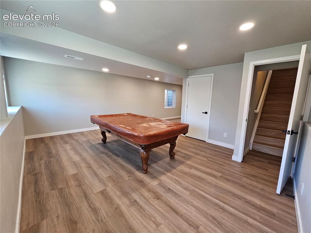 Image 19 of 26: Spacious recreation area featuring wood-finish flooring, recessed lighting,