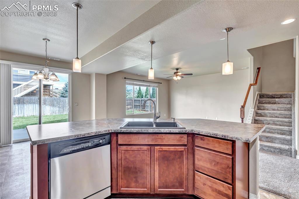 Image 10 of 50: Kitchen with stainless steel dishwasher, hanging light fixtures, brown cabi