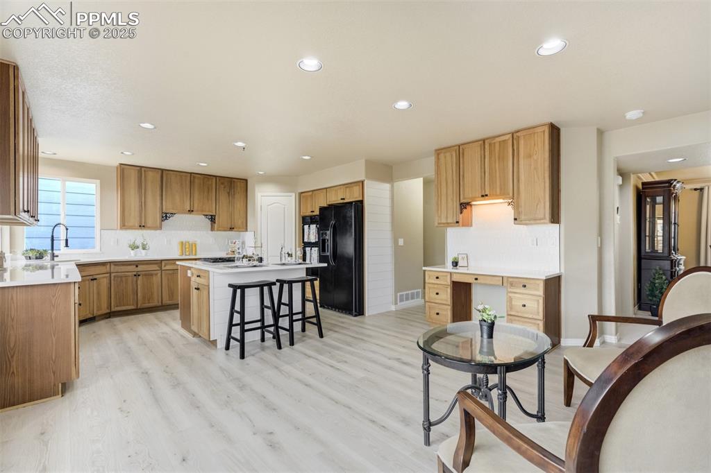 Image 10 of 50: Kitchen featuring black fridge with ice dispenser, a breakfast bar, a kitch