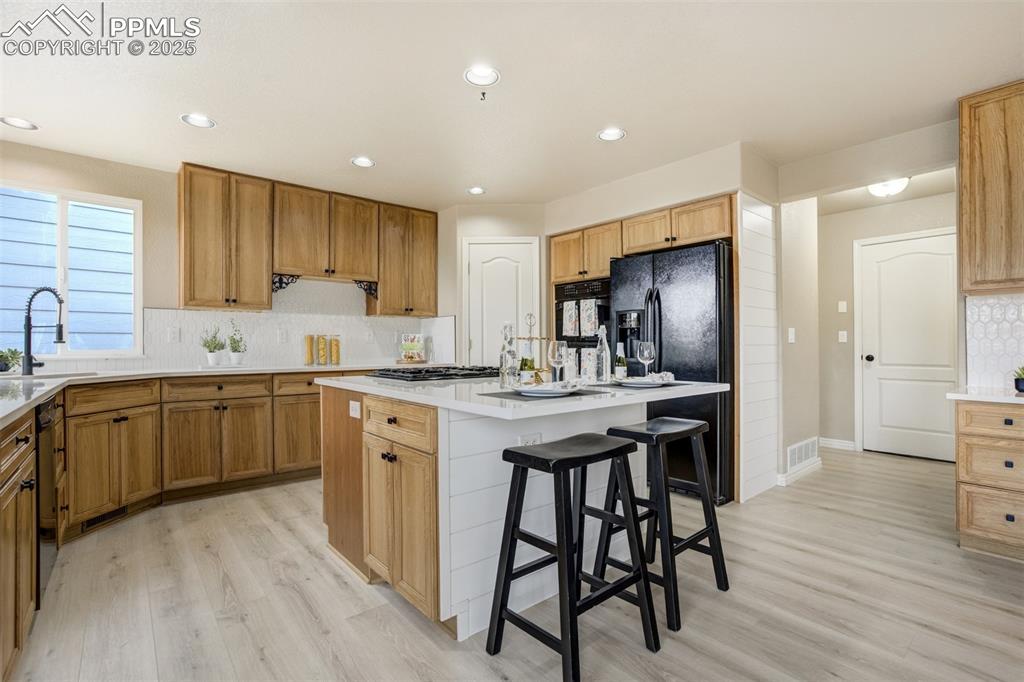 Image 11 of 50: Kitchen featuring a kitchen island, light wood-style floors, a breakfast ba