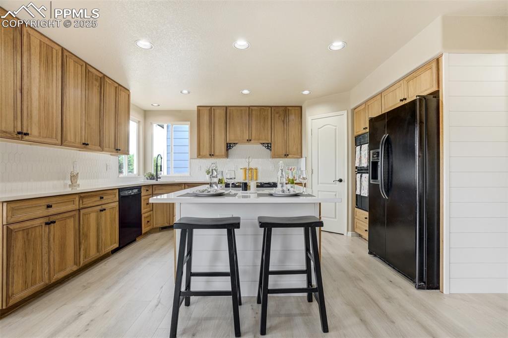 Image 12 of 50: Kitchen with black appliances, light wood-style flooring, a kitchen bar, de