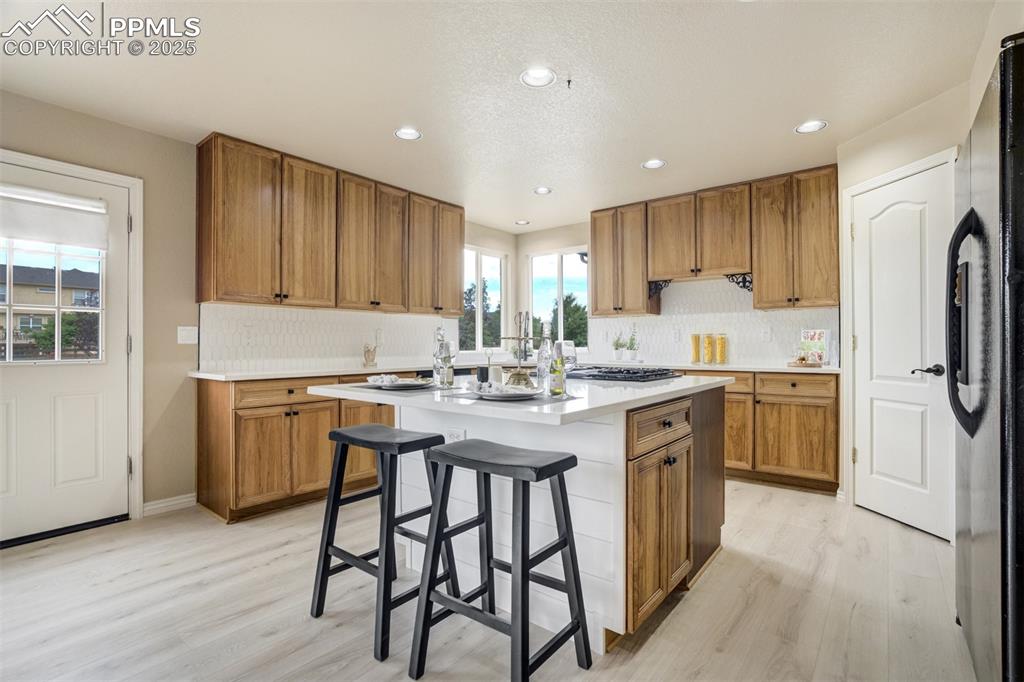 Image 13 of 50: Kitchen with light wood finished floors, brown cabinetry, a kitchen island,
