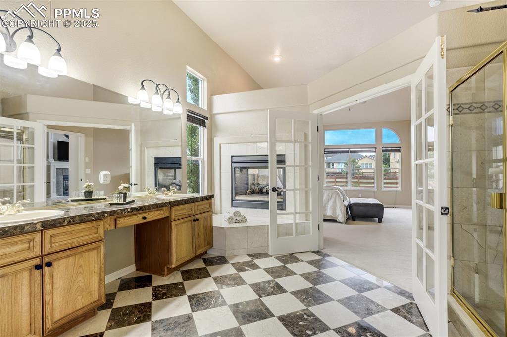 Image 24 of 50: Bathroom featuring french doors, double vanity, a tile fireplace, tiled sho