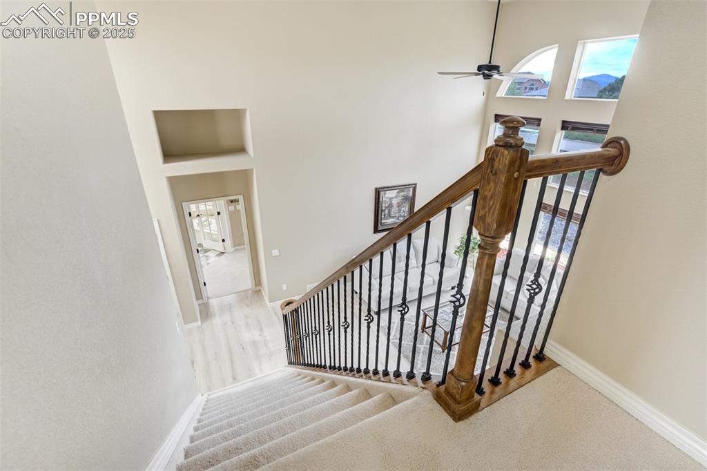 Image 26 of 50: Stairs featuring a ceiling fan, a towering ceiling, and carpet floors