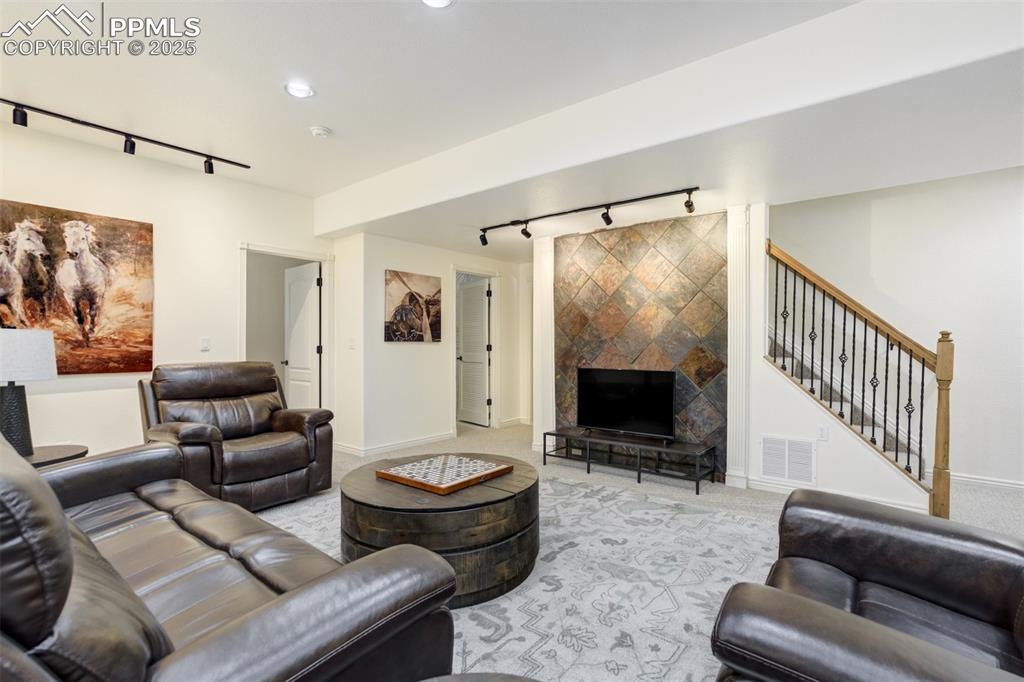 Image 38 of 50: Living room with rail lighting, a tiled fireplace, light carpet, and recess