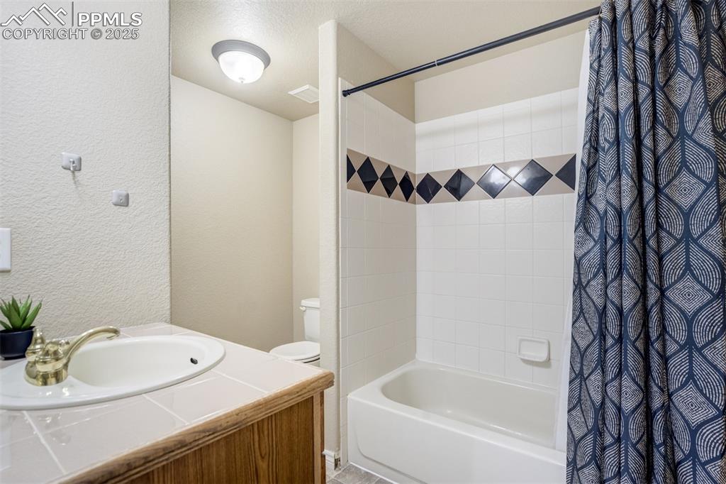 Image 44 of 50: Full bath with shower / tub combo with curtain, a textured wall, and vanity