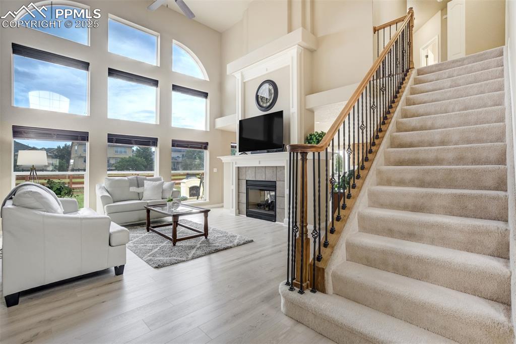 Image 6 of 50: Living room with a towering ceiling, stairway, wood finished floors, a fire