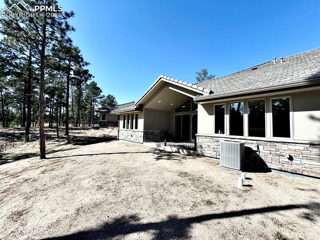 Image 28 of 33: Rear view of house with stone siding, stucco siding, and a patio area
