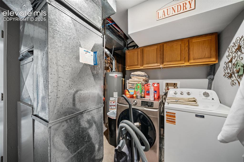 Image 30 of 50: Dedicated utility area featuring overhead wood-finish cabinetry, a laundry