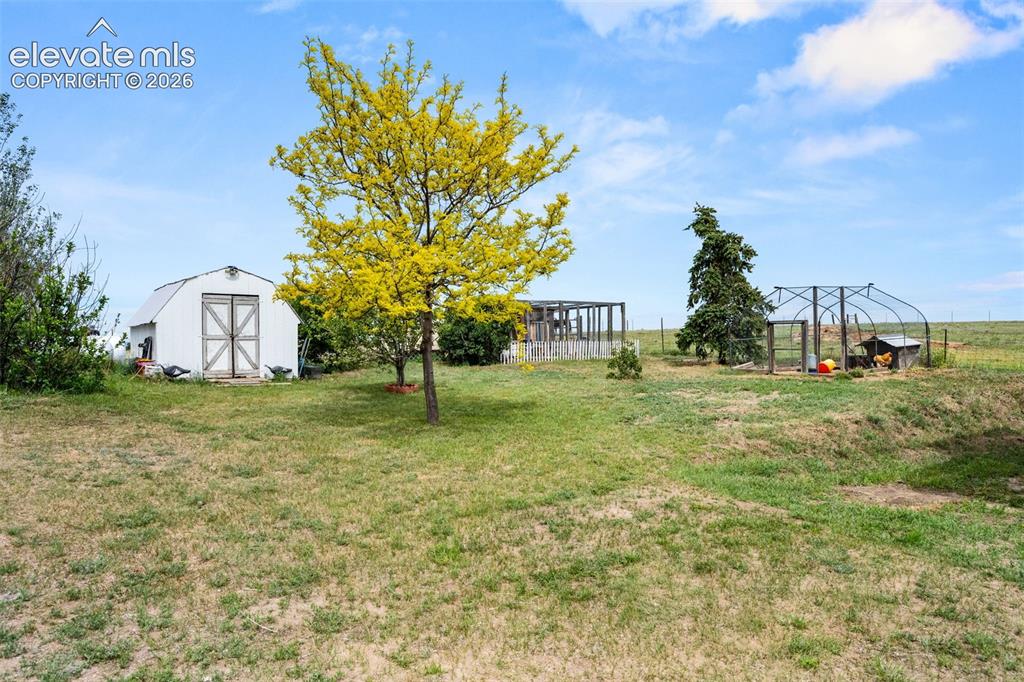 Image 36 of 50: Expansive yard featuring a white storage shed with double barn doors, matur