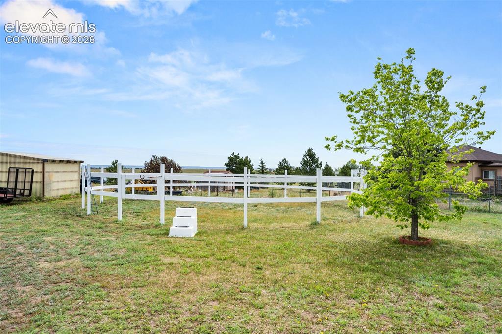 Image 38 of 50: Expansive outdoor area featuring a white perimeter fence, mature foliage, a