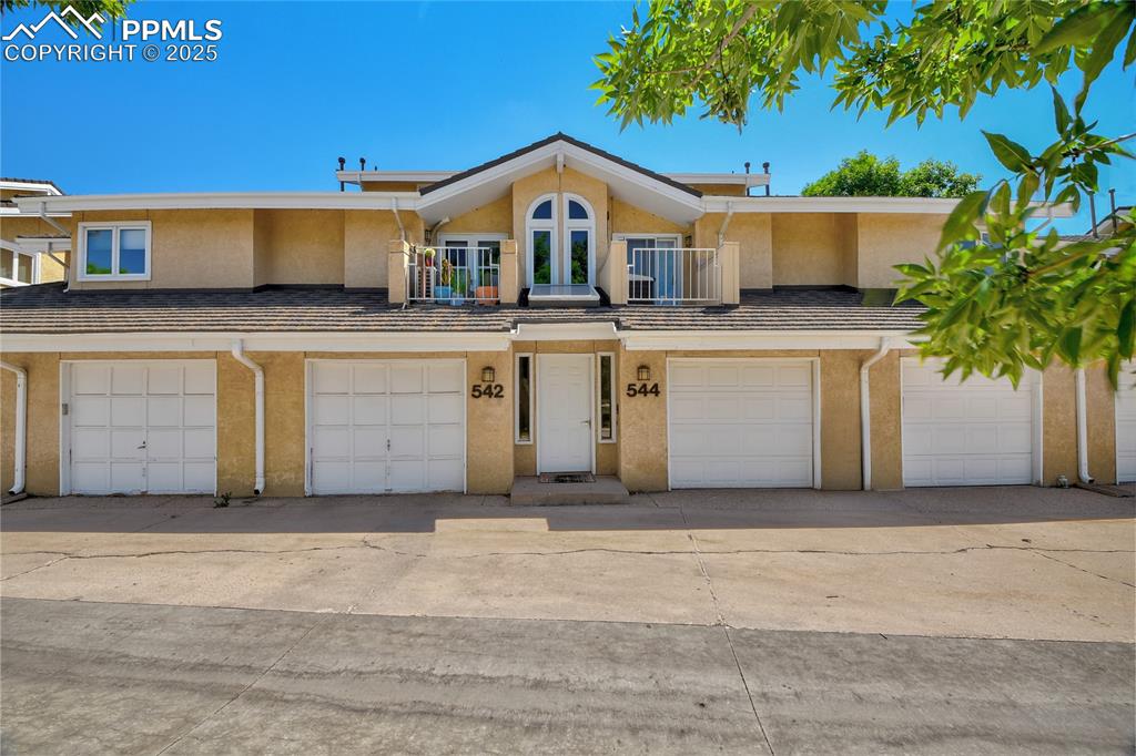 Caption: Townhome / multi-family property featuring stucco siding, a garage, a balcony, and driveway