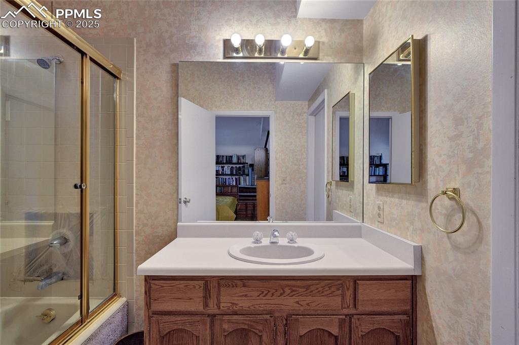 Image 13 of 22: Ensuite bathroom featuring wallpapered walls, bath / shower combo with glas