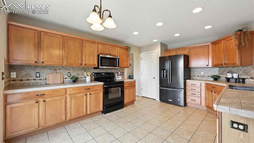 Image 14 of 50: The tiled Kitchen offers a breakfast bar, pantry, wood cabinetry, tiled cou