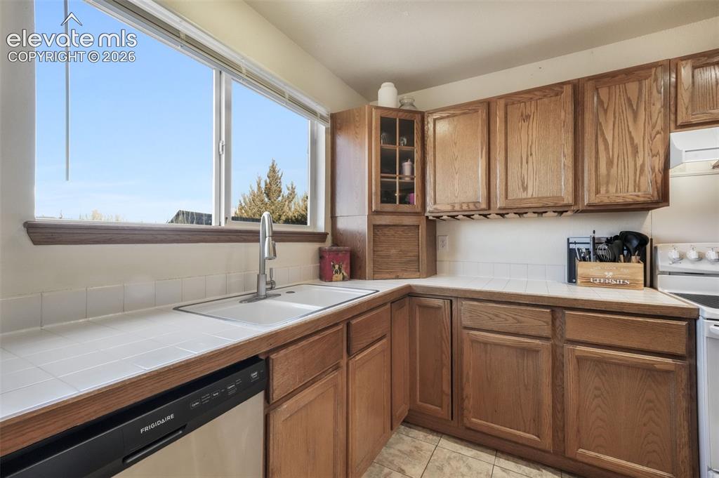 Image 13 of 50: Kitchen with wood-finish cabinetry, white tile countertops, and a full-size