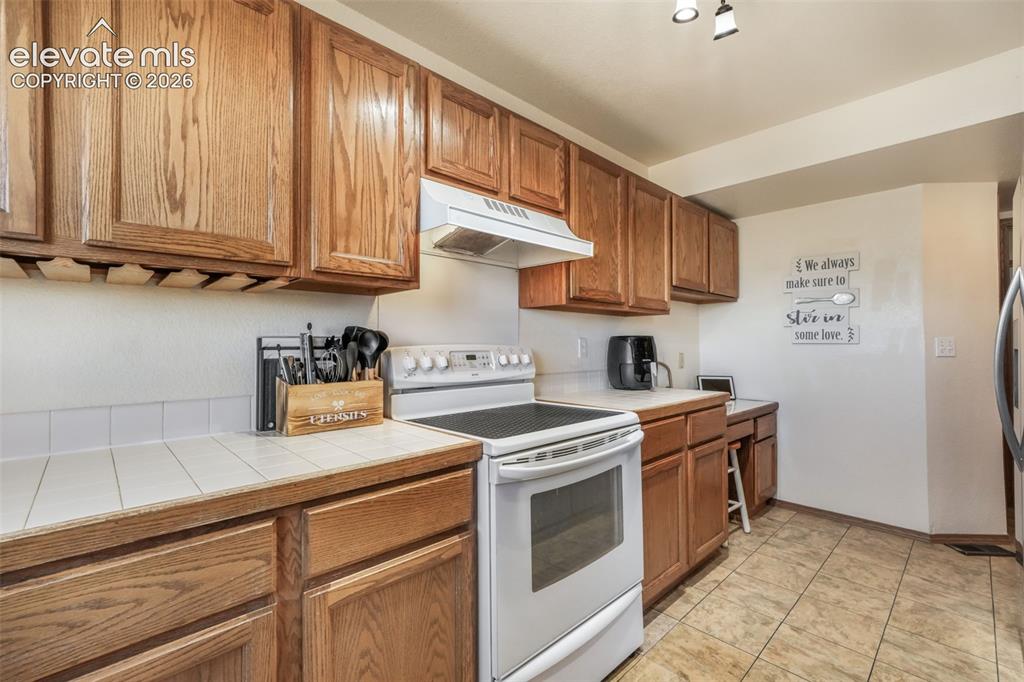 Image 14 of 50: Kitchen featuring wood cabinetry, white tile countertops, white tile backsp